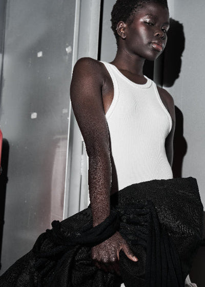 Person wearing a white tank top and black pants against a neutral background