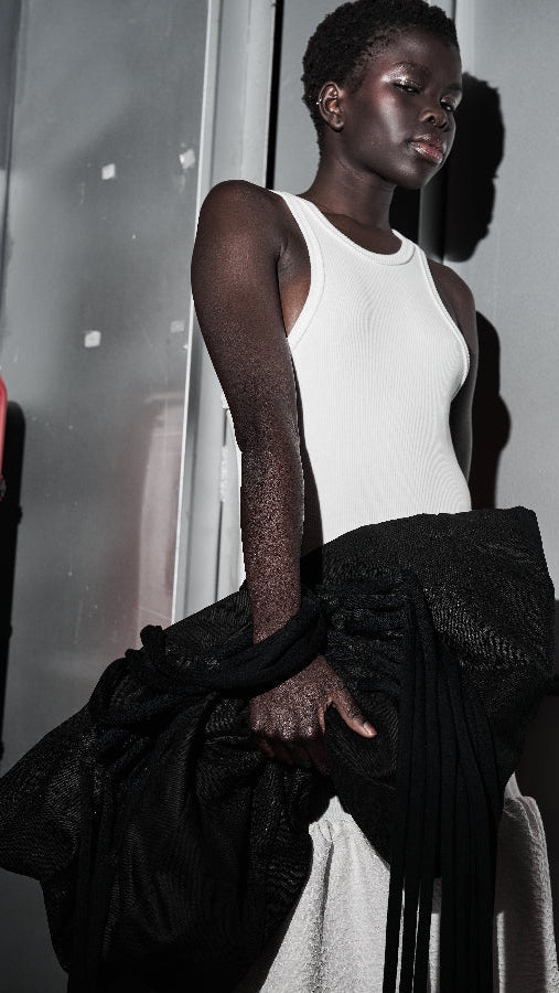 Person wearing a white tank top and black pants against a neutral background